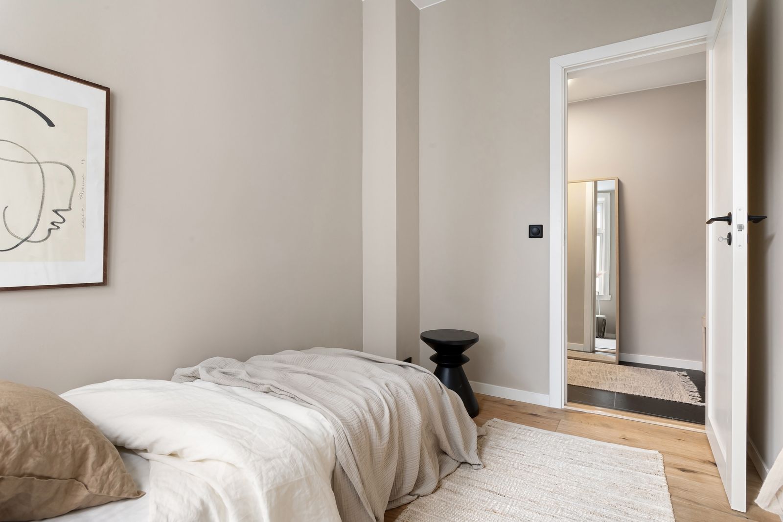 Minimal bedroom in soft neutrals with a framed line drawing, a woven throw and a mirrored doorway