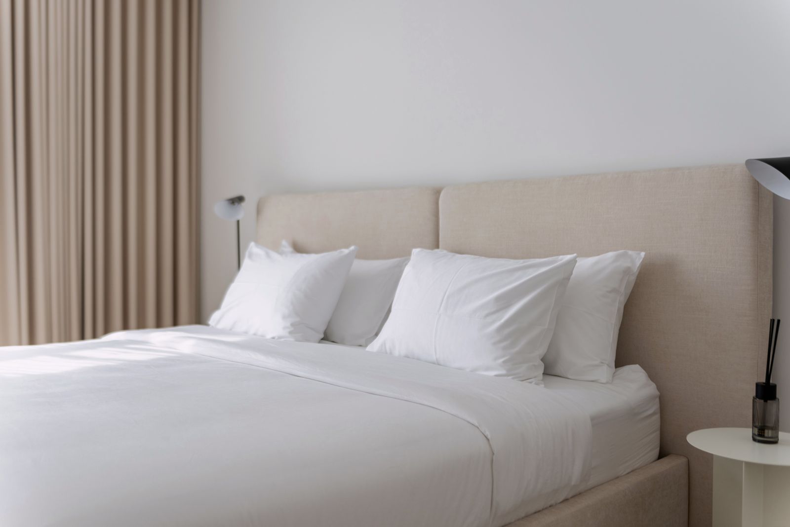 Calm bedroom with a beige upholstered headboard, crisp white linen and soft drapes