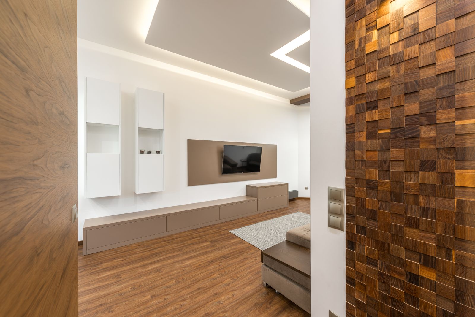 Interior detail of a timber mosaic feature wall beside a white media unit and a recessed ceiling light