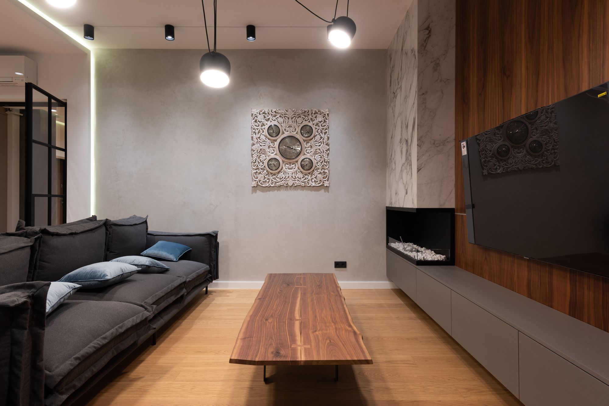 Contemporary living room with a charcoal sofa, a walnut coffee table, a textured plaster wall and a timber-clad media wall