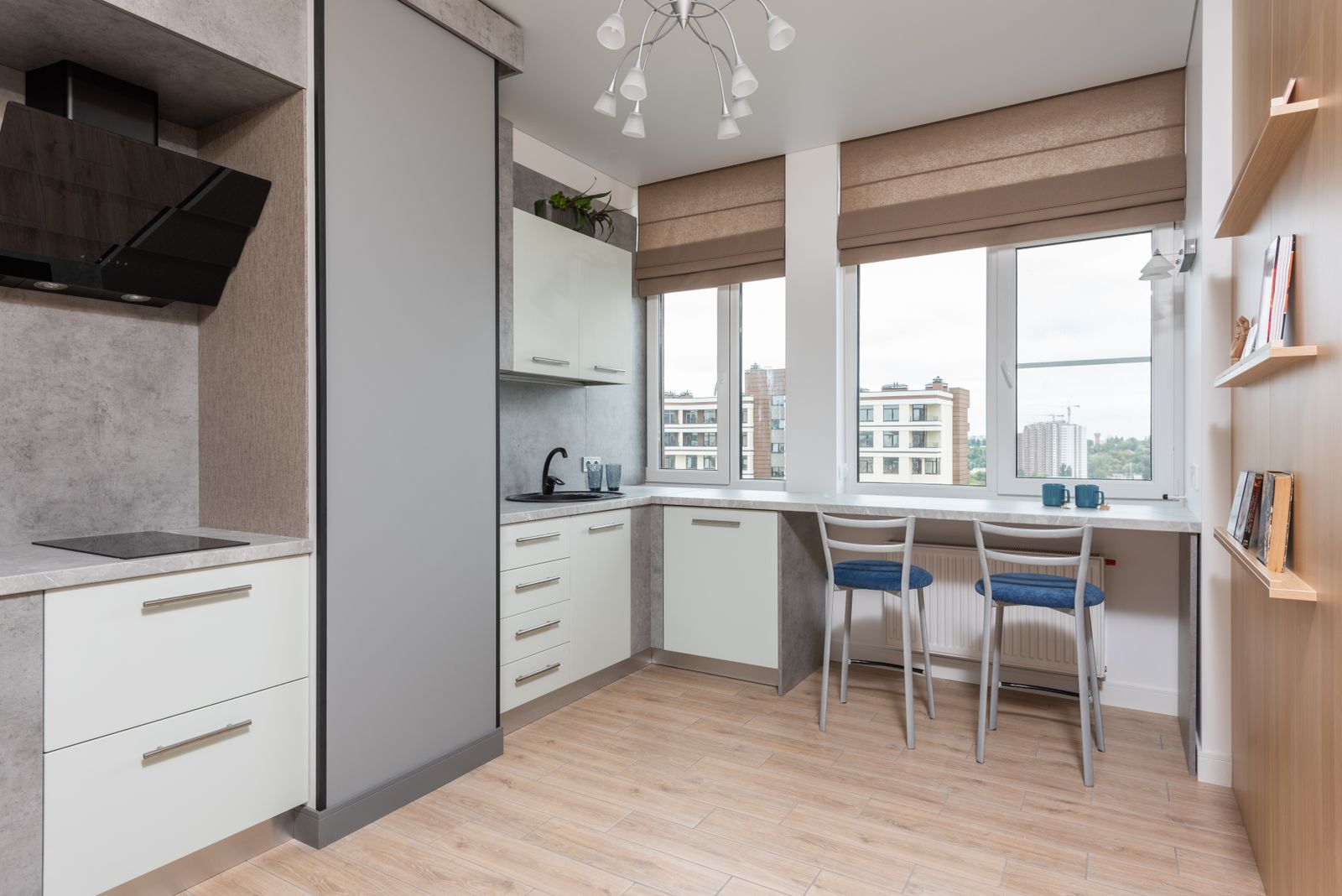 Bright L-shaped kitchen with white drawers, a stone-effect tall unit and a breakfast counter by the window