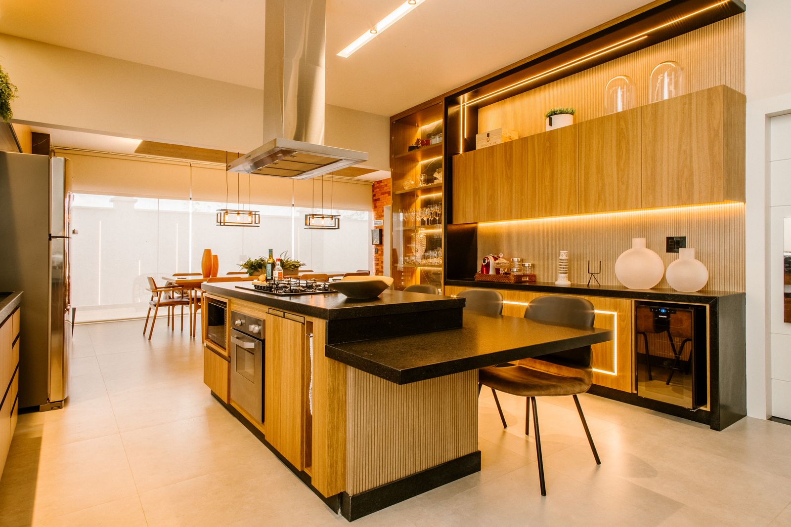 Modular kitchen with warm timber cabinetry, a black stone island, integrated lighting and an extractor hood