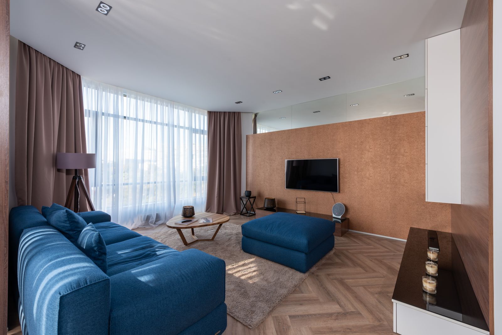 Bright living room with a blue sofa, herringbone timber flooring, a timber feature wall and floor-to-ceiling windows