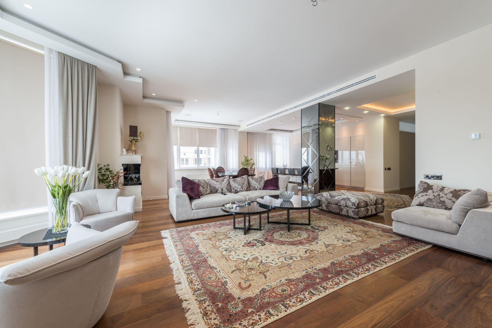Elegant living room with cream sofas and armchairs, a patterned rug and warm timber flooring