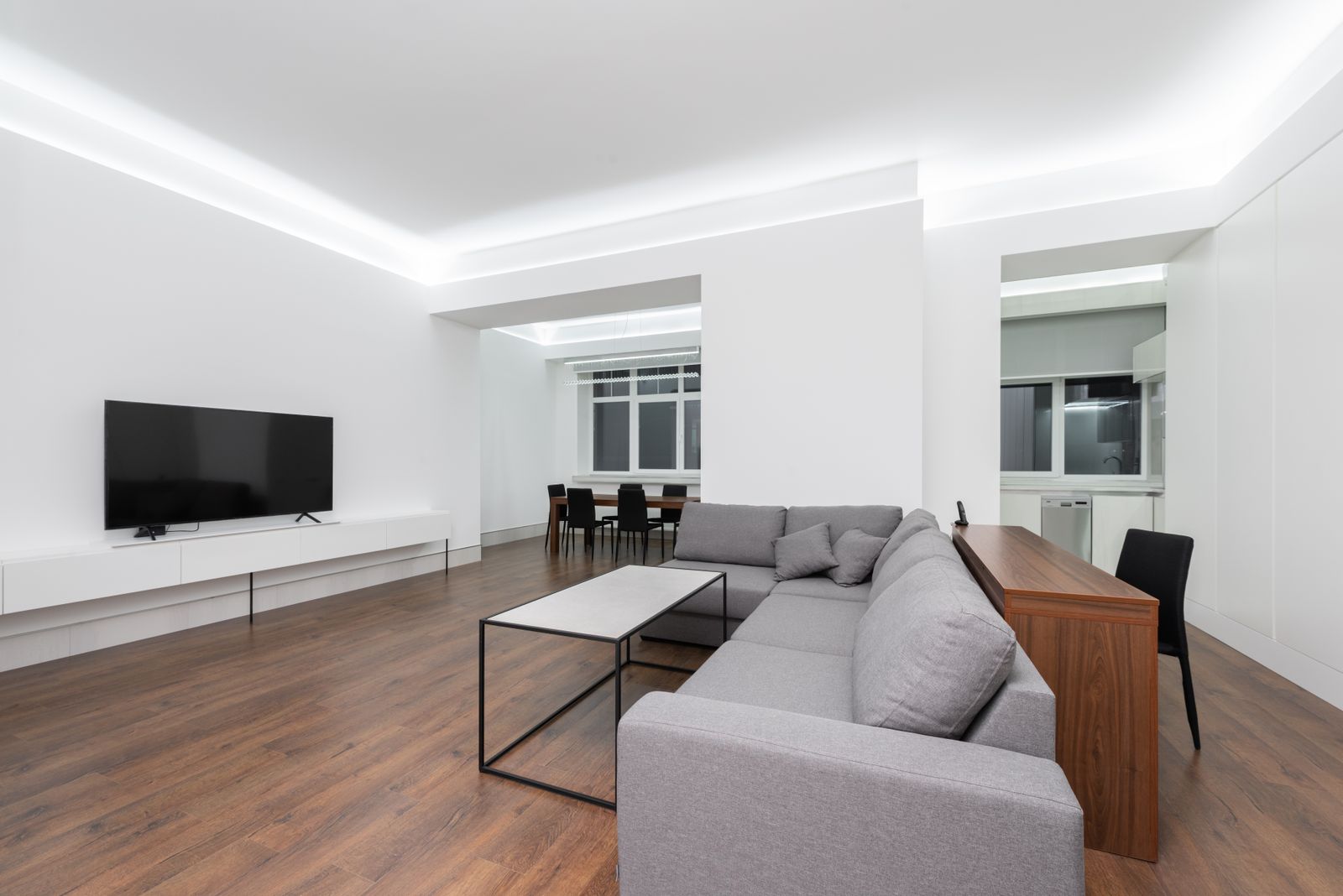 Spacious contemporary living room with a pale grey corner sofa, a walnut-topped console and a clean white ceiling cove