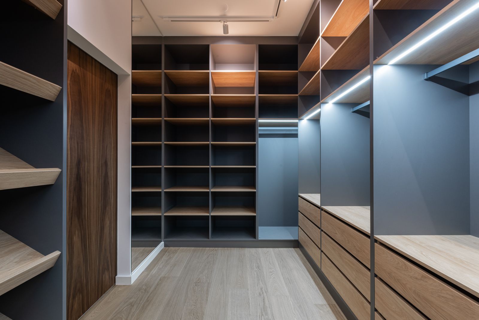 Dressing room with floor-to-ceiling open shelving, a central island of drawers and a dark walnut door